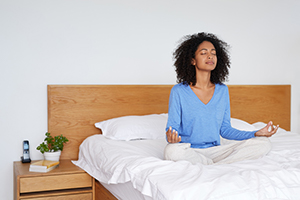 Young woman sitting cross-legged in bed meditating 