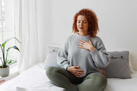 Woman sitting on a bed practicing breathing.