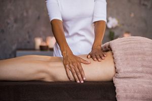 A massage therapist works on a prone client's upper leg.