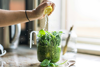 Lemon juice is squeezed into a measuring cup over green, leafy vegetables.