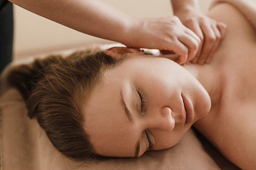 A woman lying on a table receiving a neck massage from a massage therapist. 
