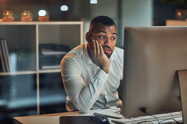 Man slouching in front of computer with his chin in hand