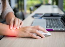 A hand on a mouse next to a computer with glowing red light on the wrist showing wrist pain