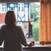 Woman with her back to the camera looking out the window with a cup of tea