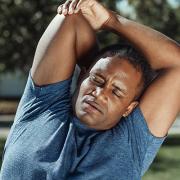 African American man stretching with one arm behind his back.