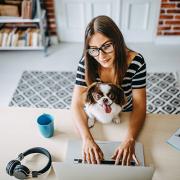 Woman working at a home computer with a dog on her lap
